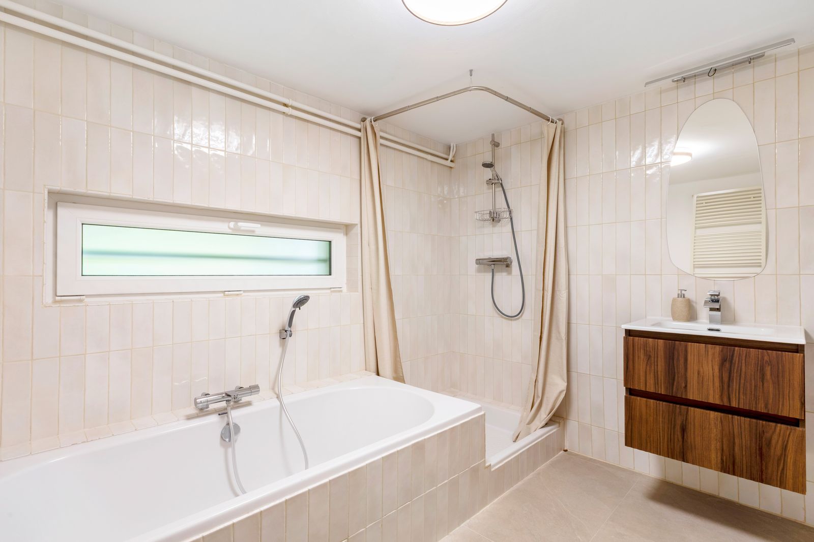 Salle de bains avec baignoire, carrelage beige et meuble en noyer