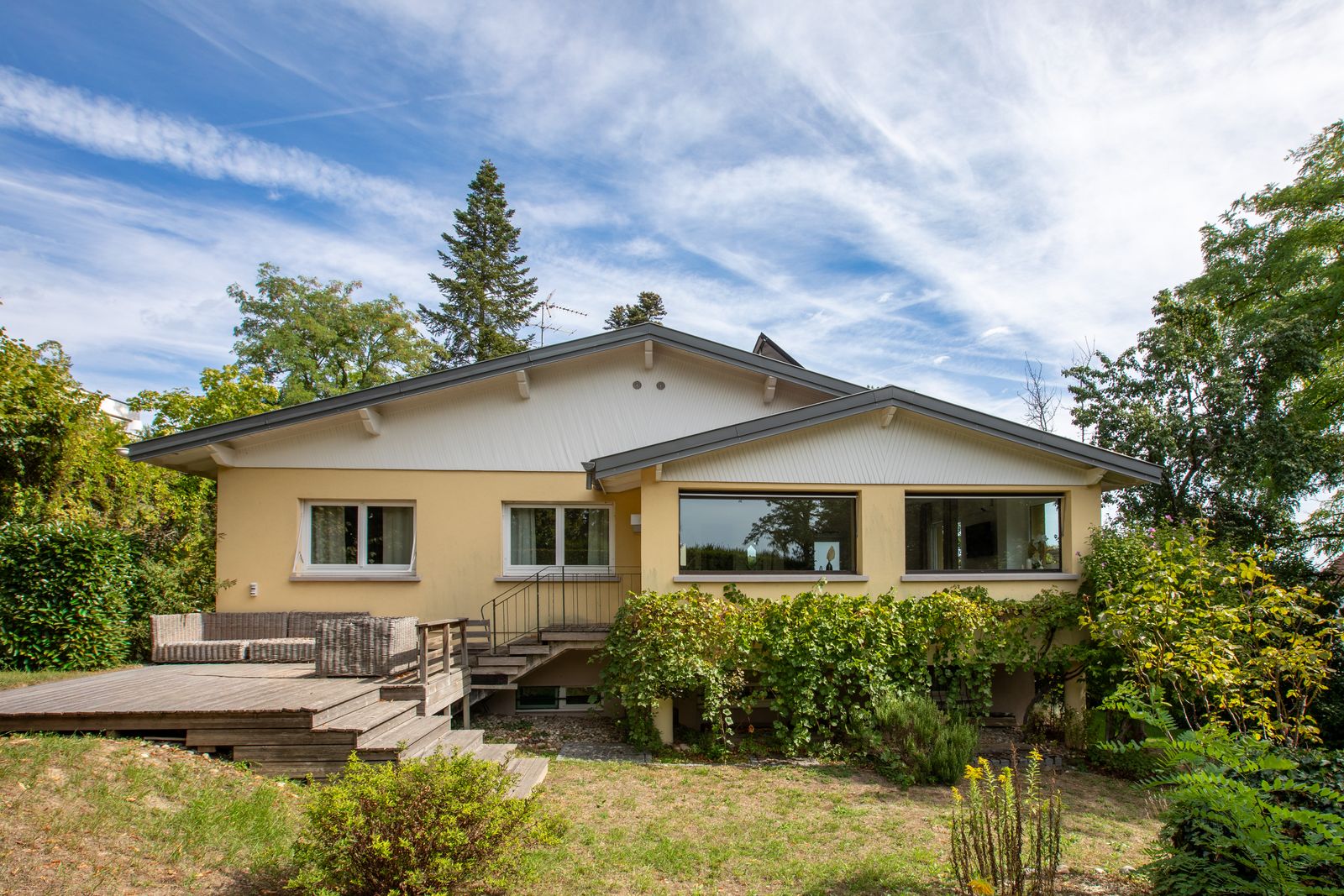 La villa vue du jardin, sa terrasse en bois et sa façade ocre sous les arbres