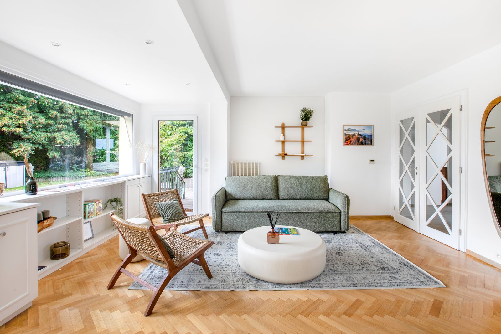 Le salon : canapé vert sauge, table basse ronde et fenêtres sur le jardin